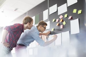 two men in front of work board with stick notes