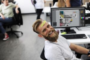 man sitting at an office desk with a sticky note on his forehead