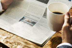 hands holding newspaper and coffee at desk