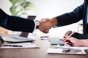 professionals in suits shaking hands over desk