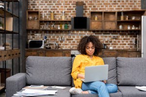 Black woman sitting on a couch on her computer. 